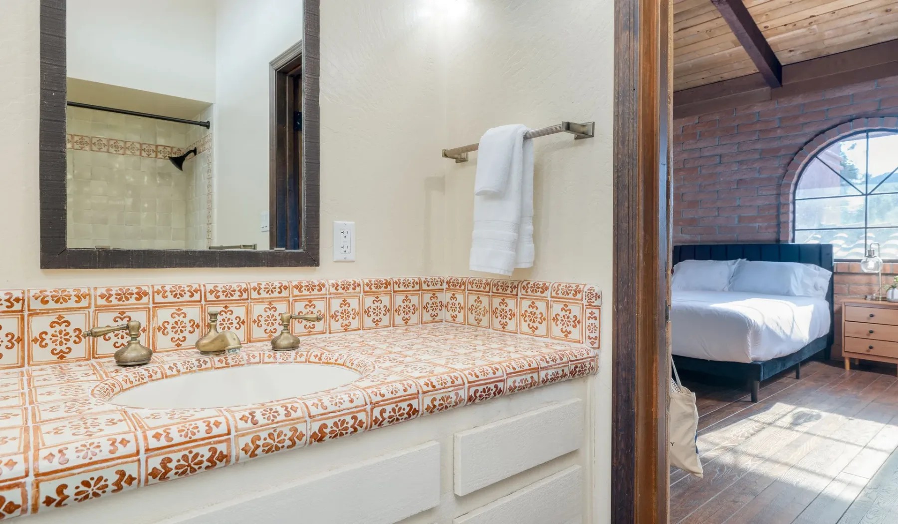 Un lavabo de baño con azulejos da a un dormitorio con una cama y una ventana arqueada.