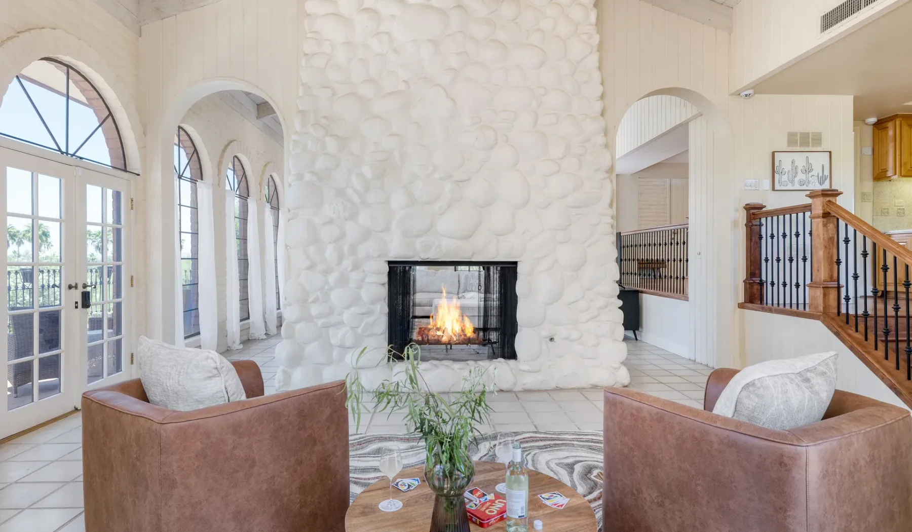 Una sala luminosa con una chimenea de piedra y ventanas arqueadas.