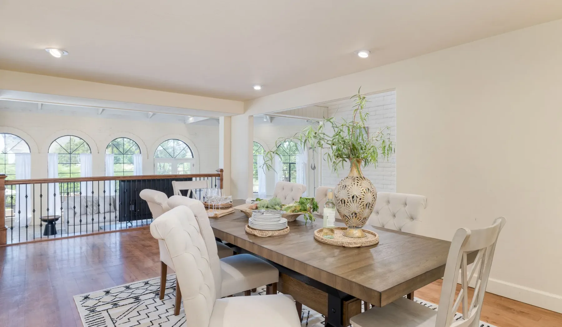 Un comedor luminoso con una mesa de madera junto a ventanas altas con arcos.