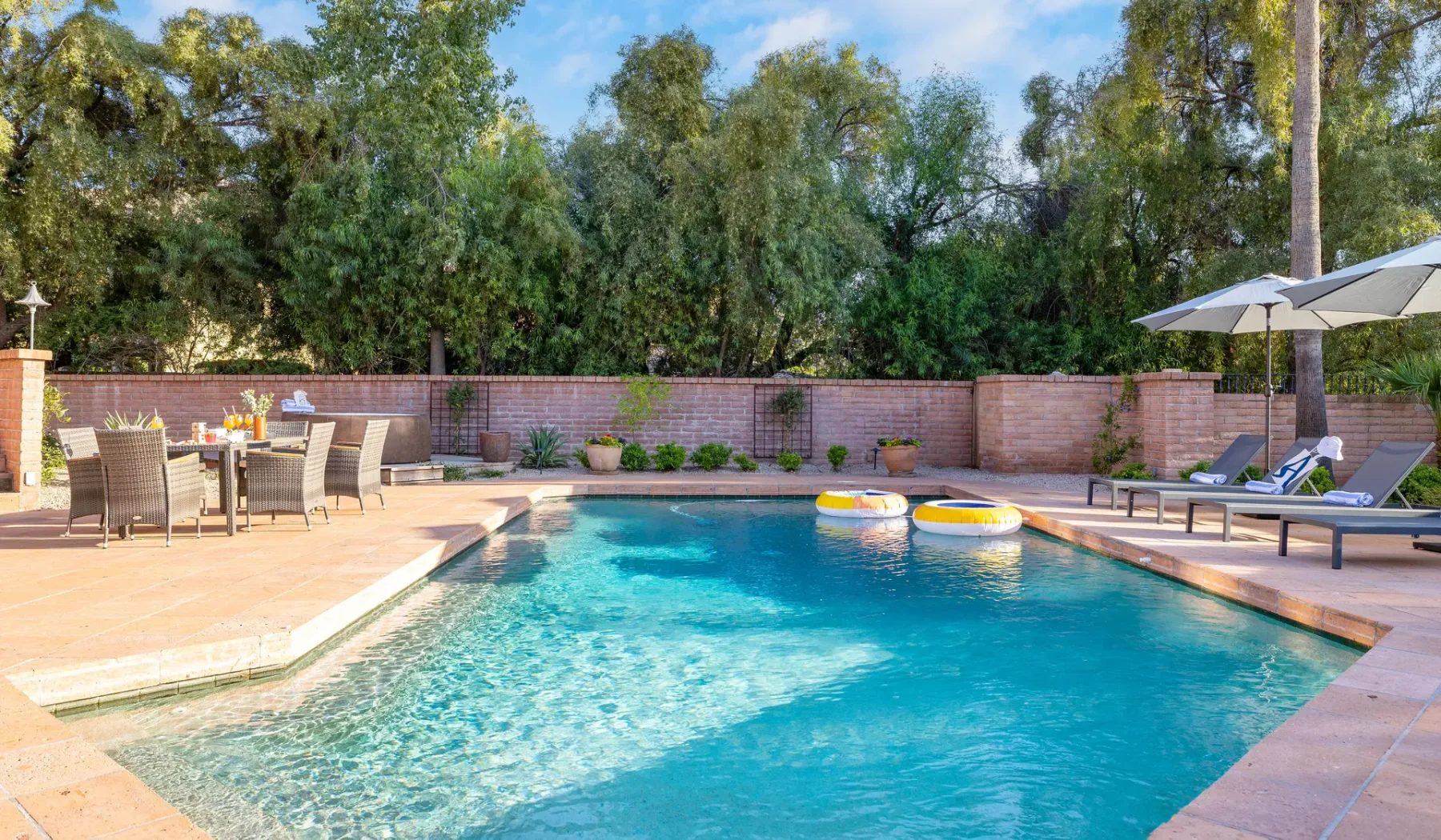 Una piscina al aire libre junto a un patio pavimentado con asientos y sombrillas.