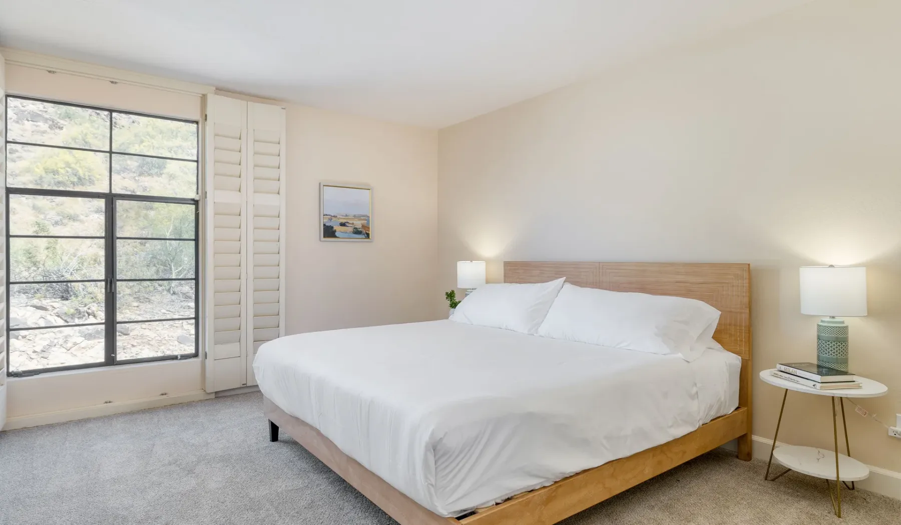 Un dormitorio luminoso con una cama grande y una ventana amplia con vistas a los árboles.