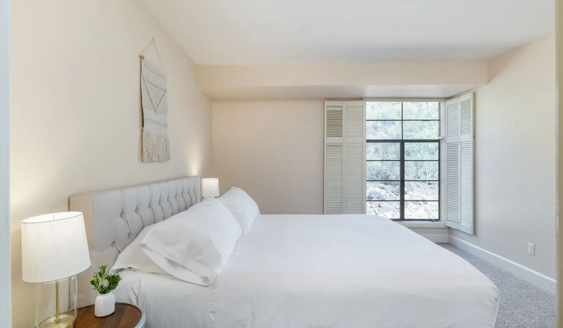 Un dormitorio luminoso con una cama grande y una ventana con contraventanas abiertas.