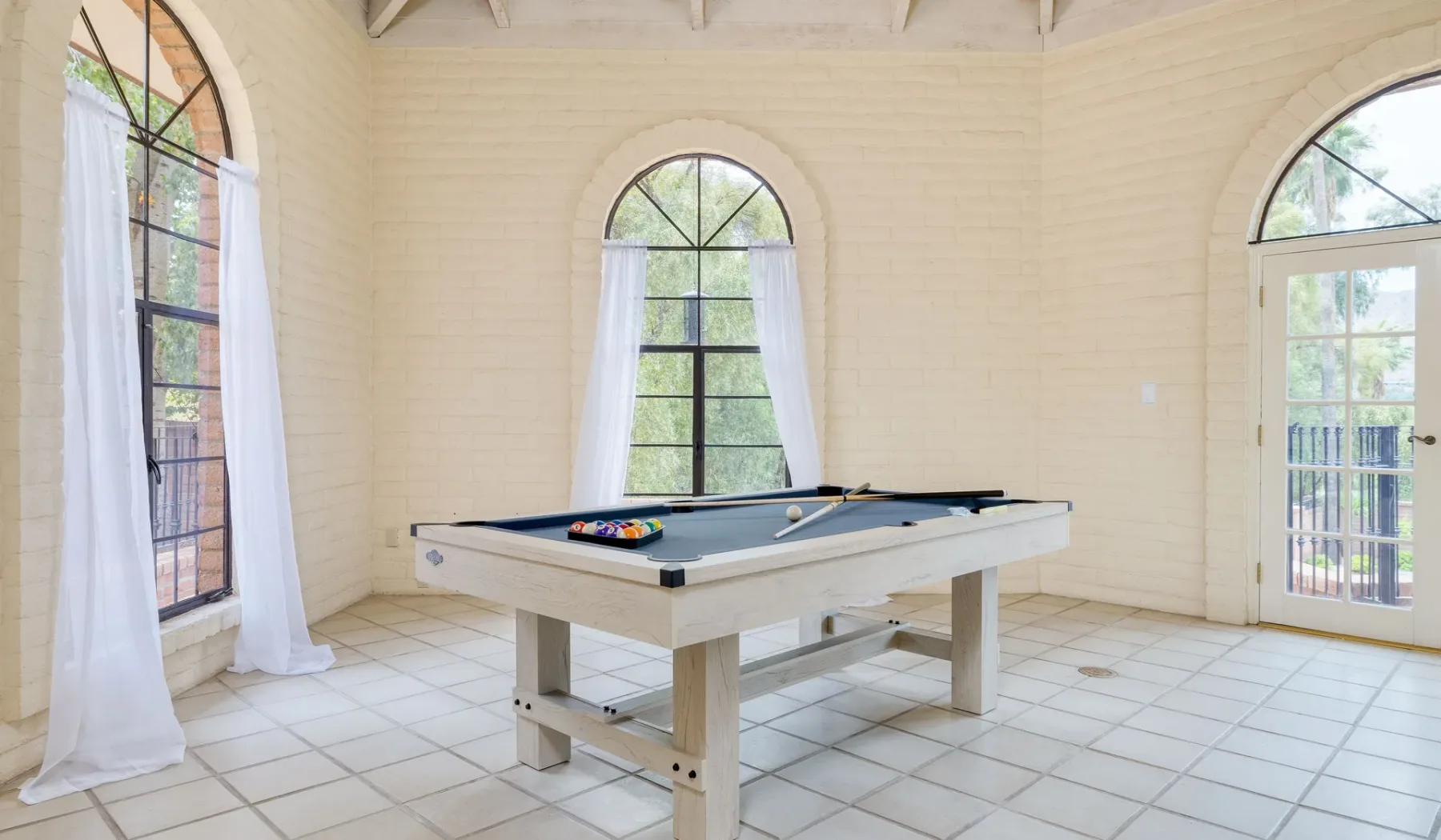 Una mesa de billar está en una habitación luminosa con ventanas altas y arqueadas.
