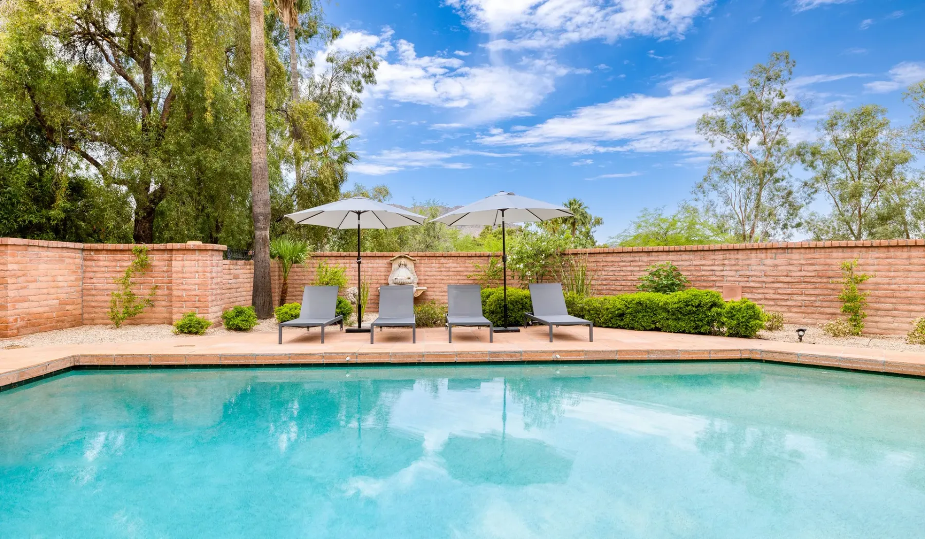 Una piscina al aire libre con asientos reclinables y sombrillas junto a un muro de ladrillo.