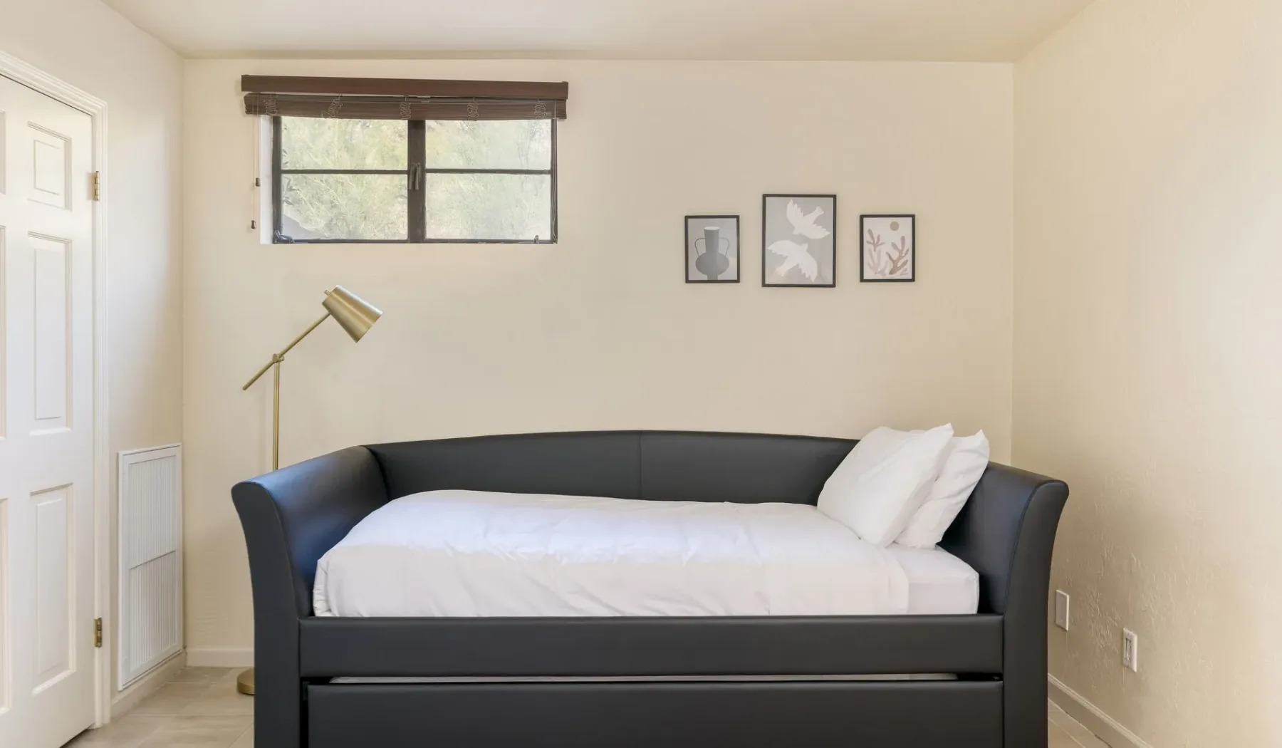 Un dormitorio con una cama, una ventana pequeña y cuadros en la pared.