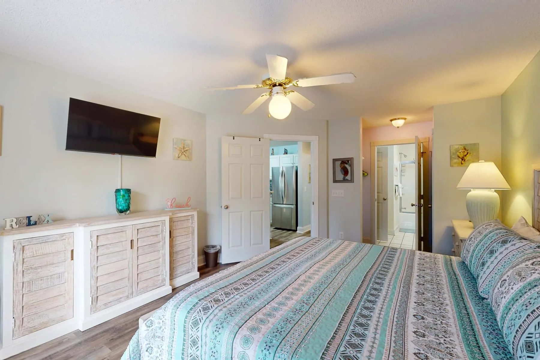 A bedroom with a patterned bedspread, white storage cabinets, and a ceiling fan.