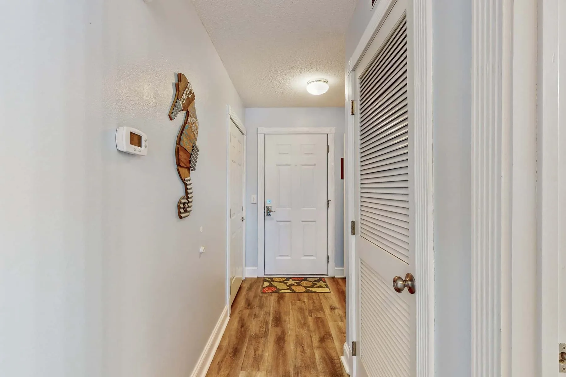 A narrow hallway with wood-look flooring leads to a white door.