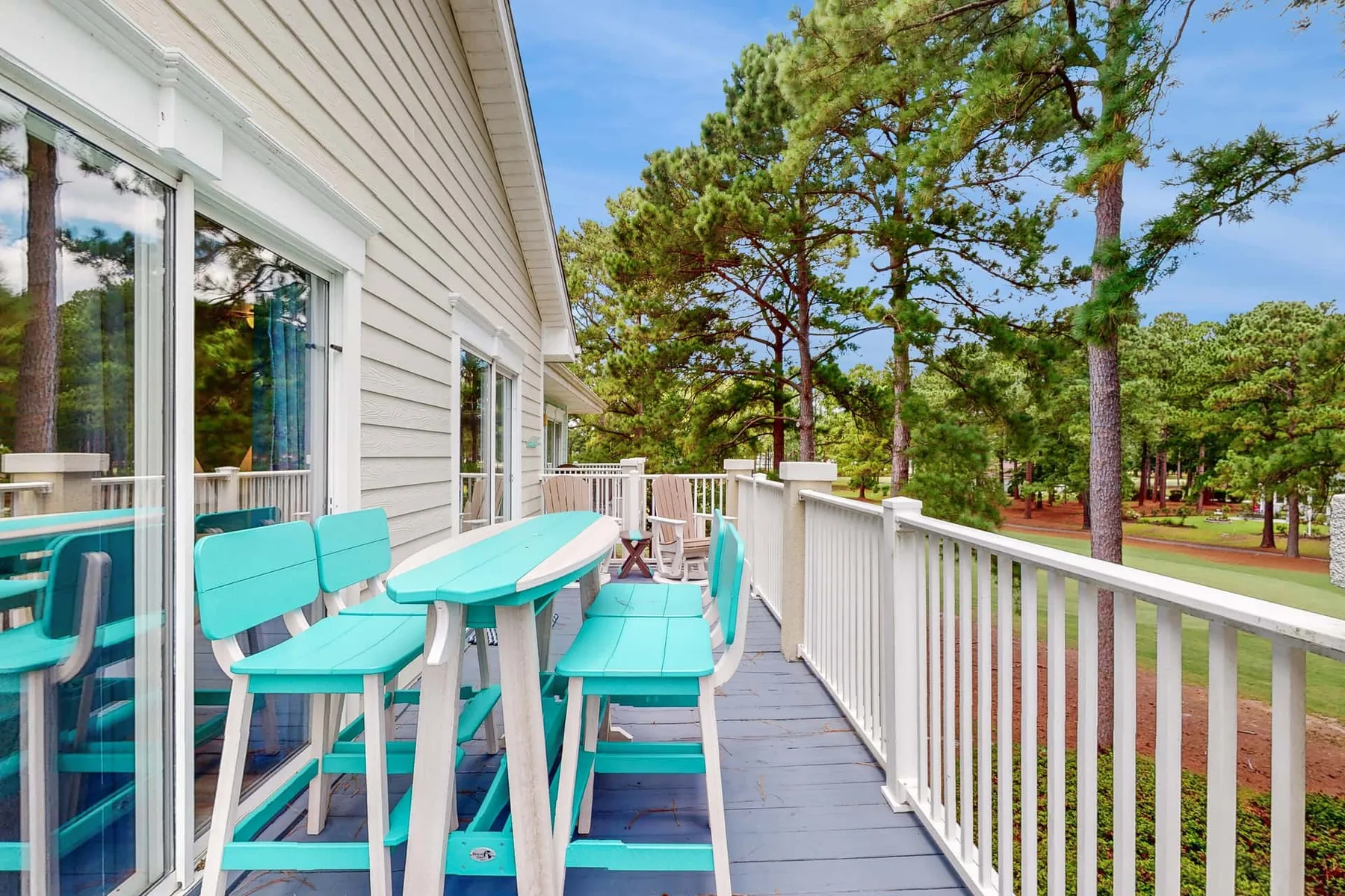 An outdoor deck has turquoise seating beside a white railing, with pine trees beyond.