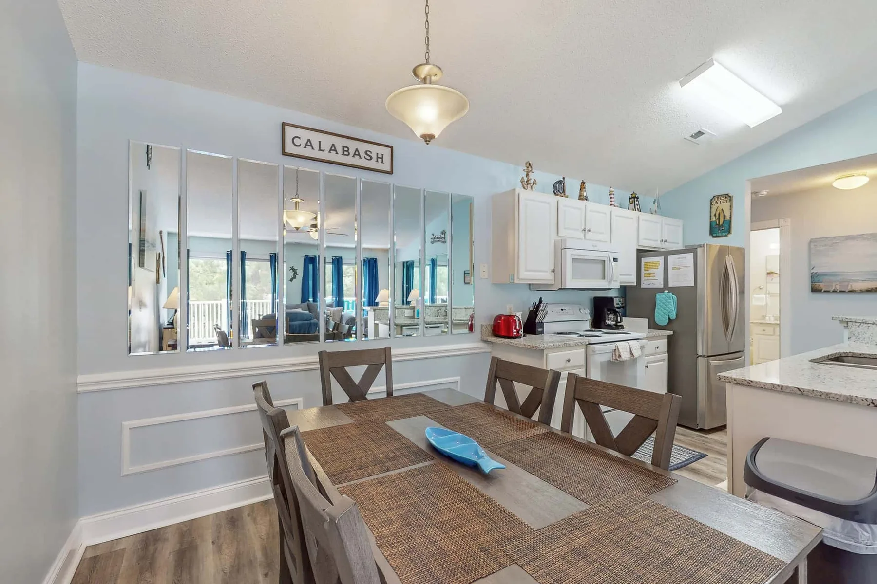 A dining area with a long table beside a bright kitchen.