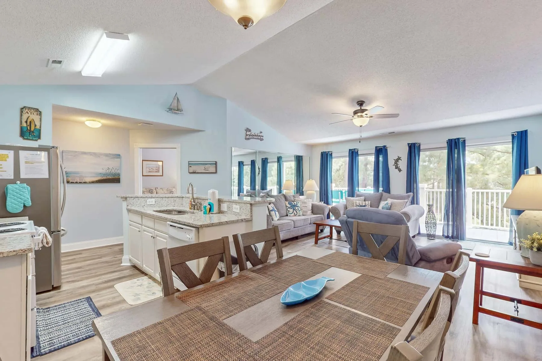 An open-plan dining and living area with a kitchen island and blue curtains.