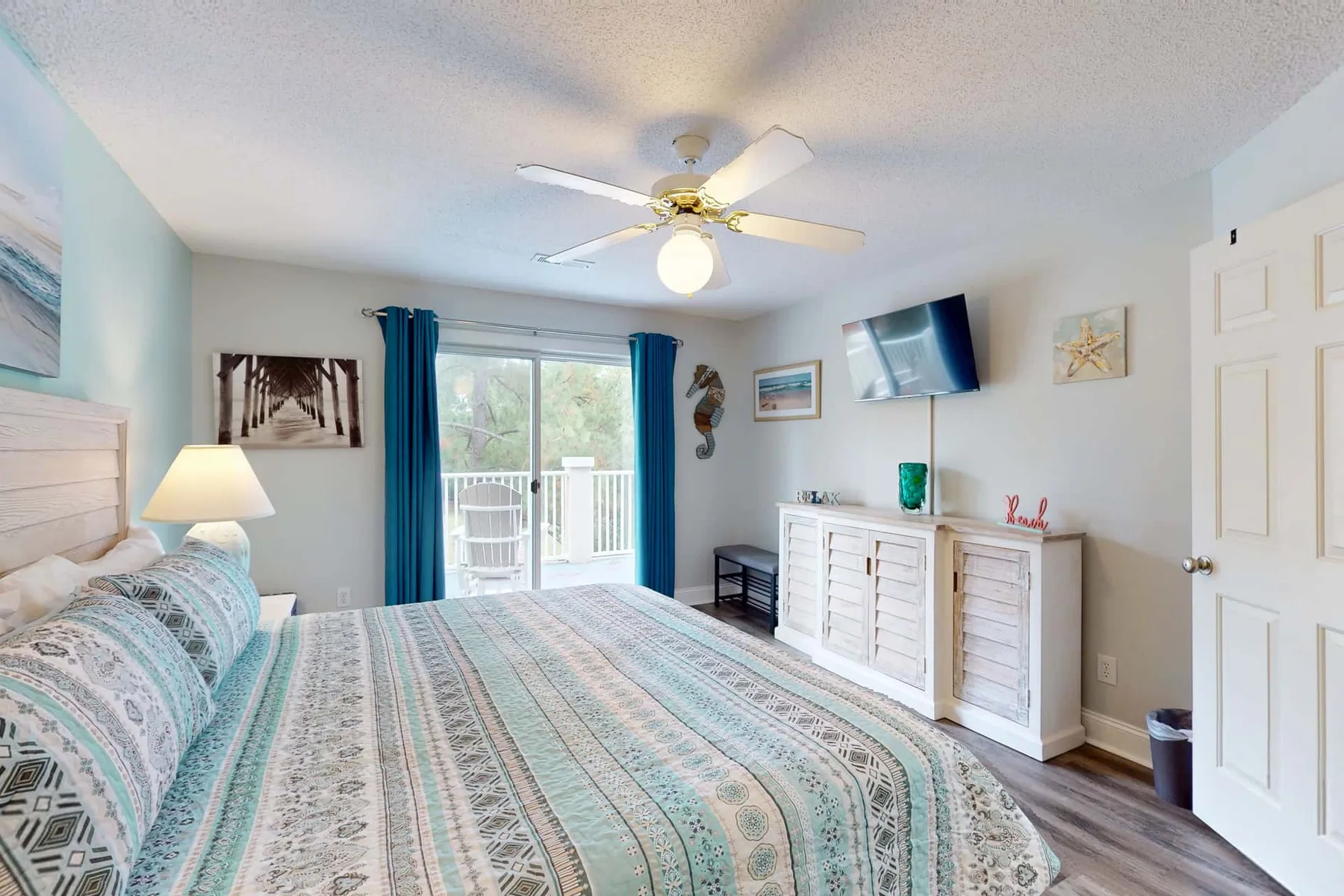 A bedroom with a patterned bedspread, sliding glass doors, and a white dresser.