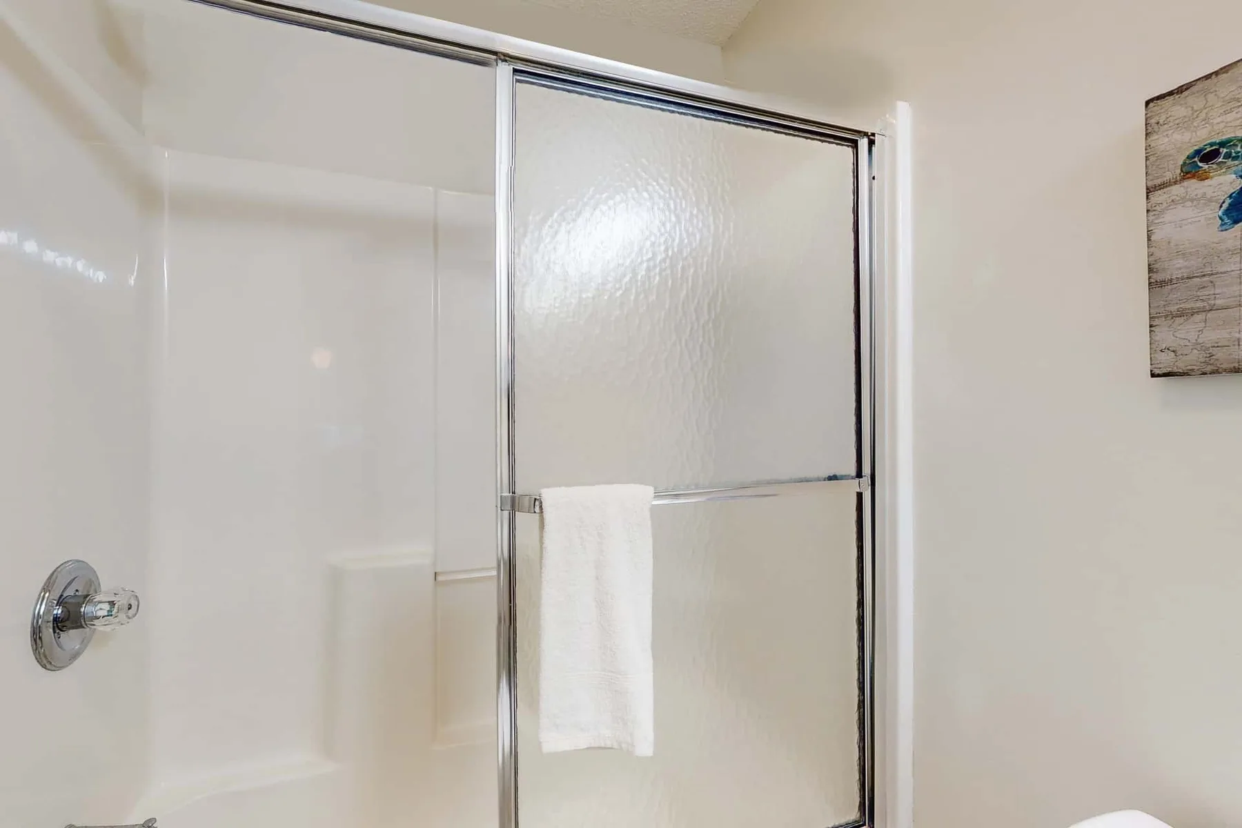 A bathroom shower with a white towel hanging on the glass panel.