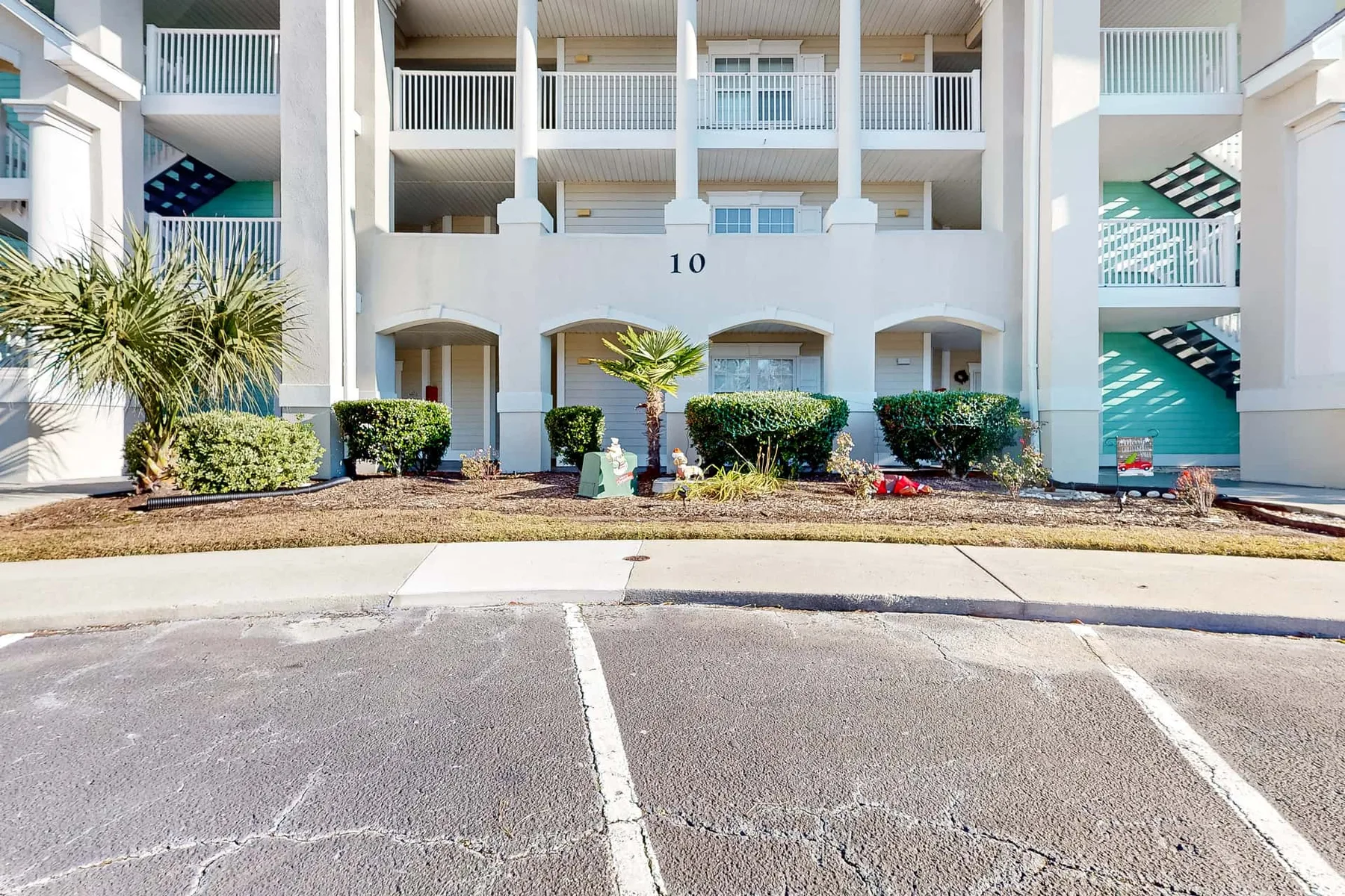 A white multi-story building with balconies faces a paved parking area.