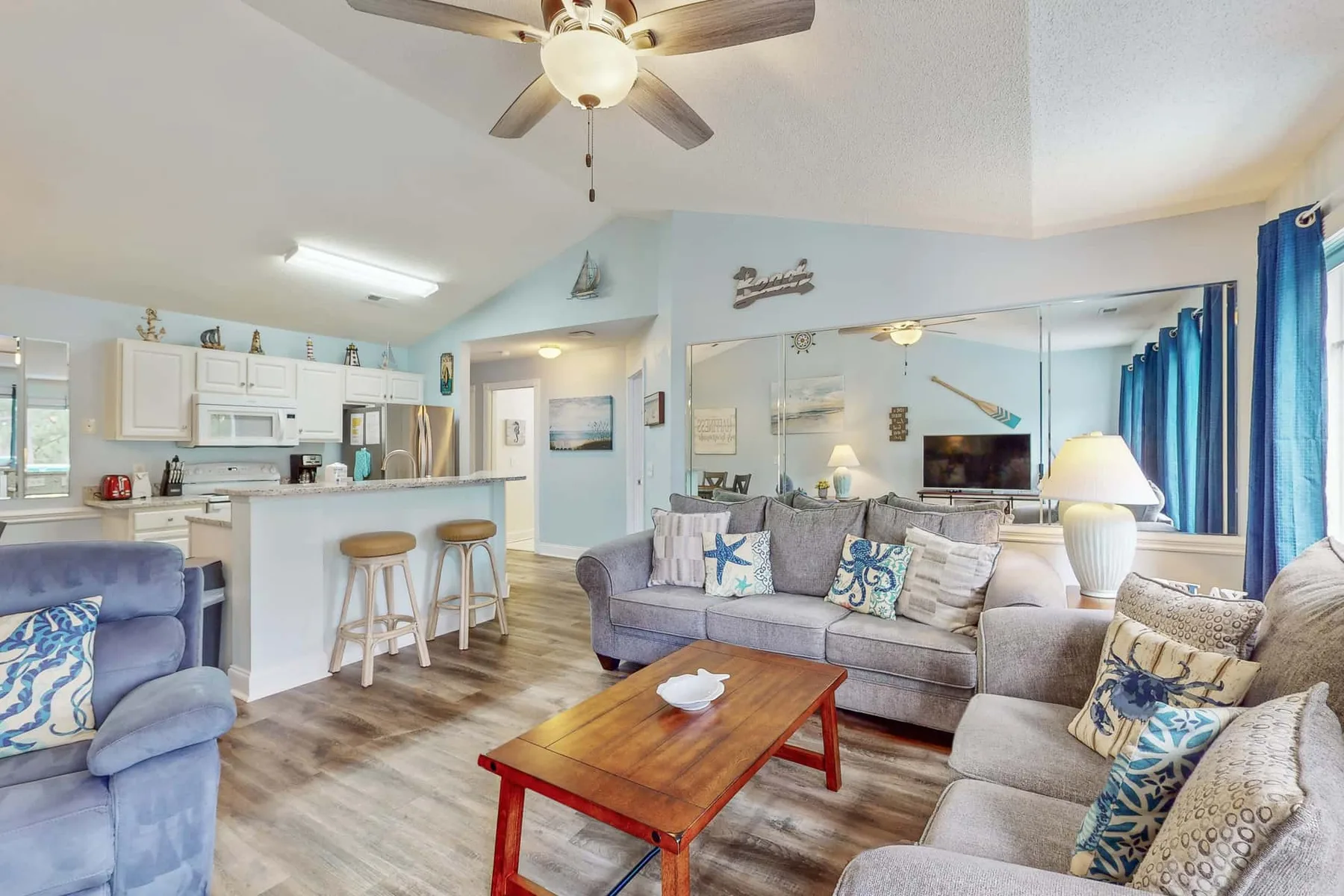 A living room with gray seating, a wooden coffee table, and an open kitchen.