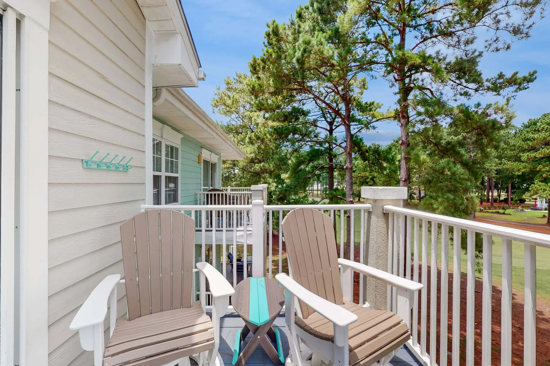 A wooden deck with two outdoor chairs overlooks a tree-lined area.