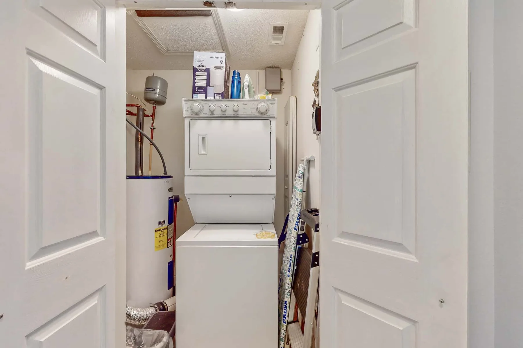 A laundry closet with a stacked washer and dryer between open doors.