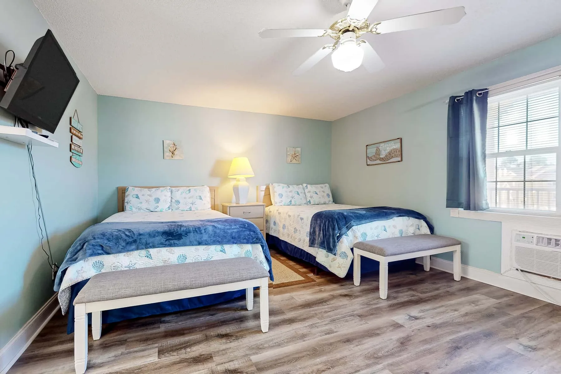 A bedroom with two beds, a small table, and a window with blue curtains.