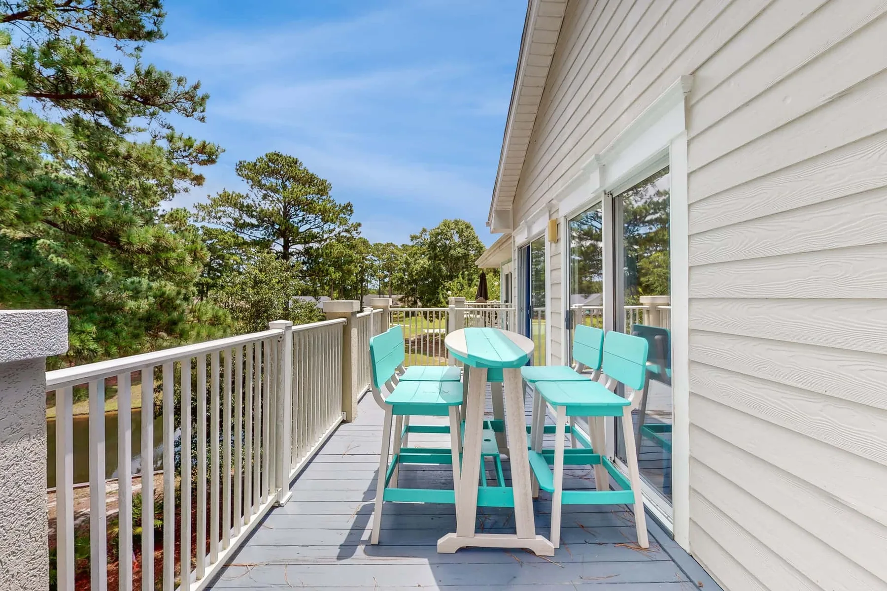 A deck with turquoise seating and a table overlooks a wooded landscape.