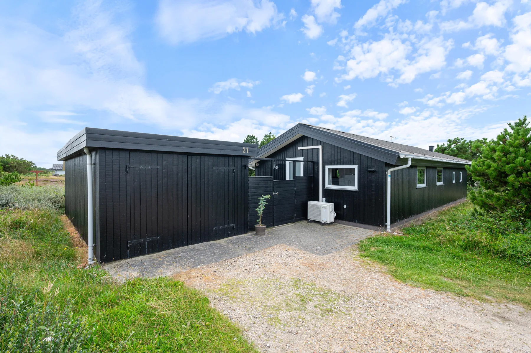 A dark exterior building stands beside a gravel driveway and grassy yard.
