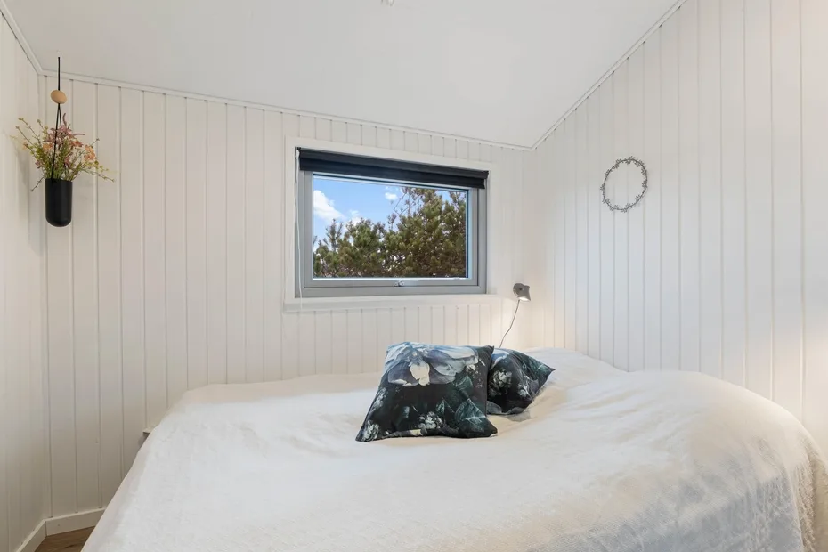 A bright bedroom with a bed beneath a window.