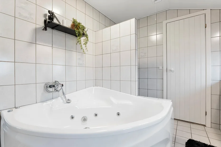 A tiled bathroom with a large corner bathtub and wall-mounted shelf.