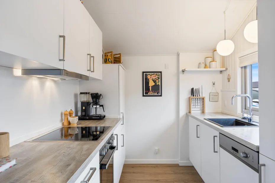 Una cocina blanca y luminosa con encimeras, una placa de cocina y un fregadero.
