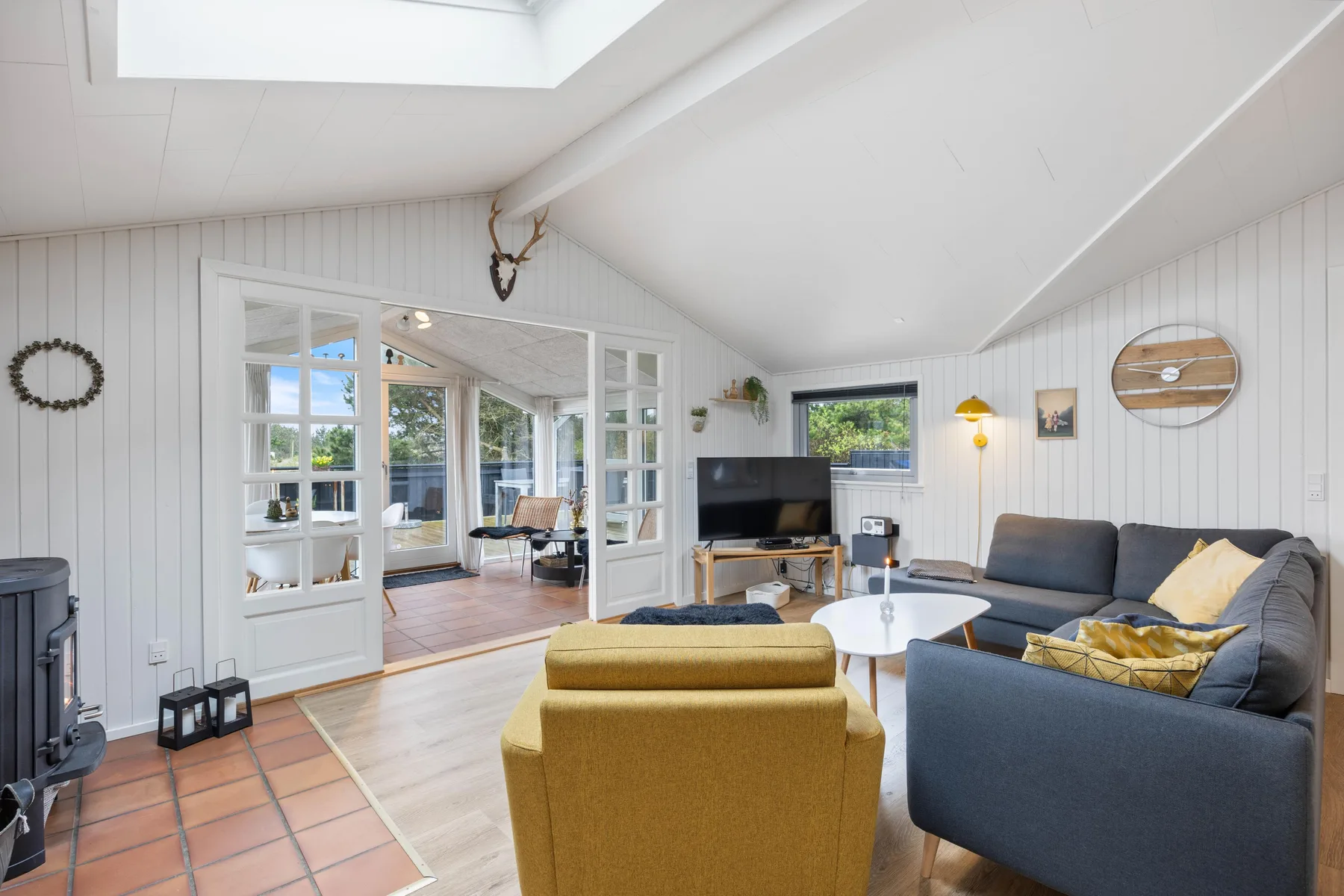 A bright living room with seating around a coffee table and glazed doors opening to another space.