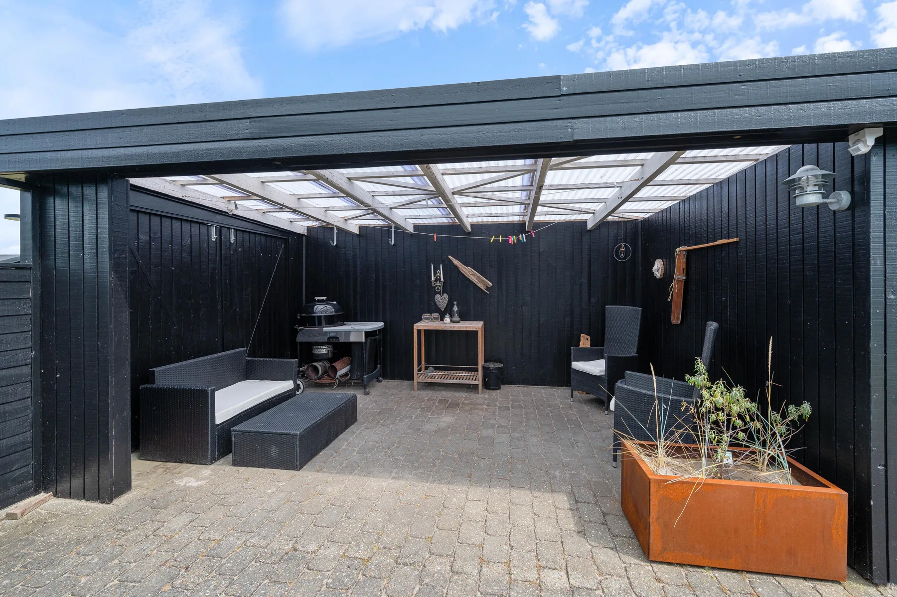 A covered outdoor patio with dark walls, seating, and a planter.