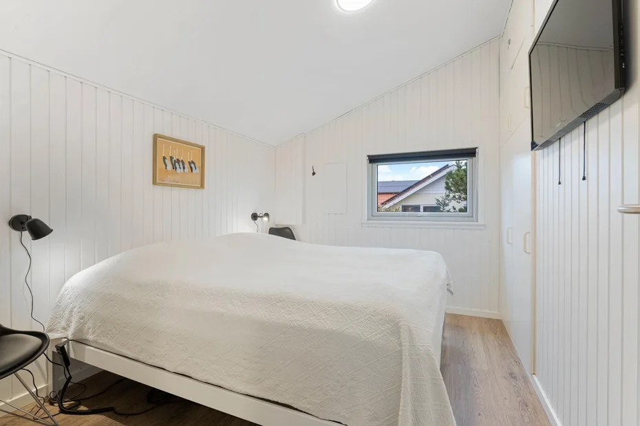 A bright bedroom with a bed, a window, and a wall-mounted television.