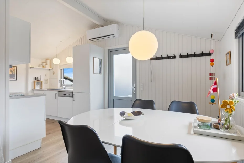 A bright dining area with a white table and an adjoining kitchen.