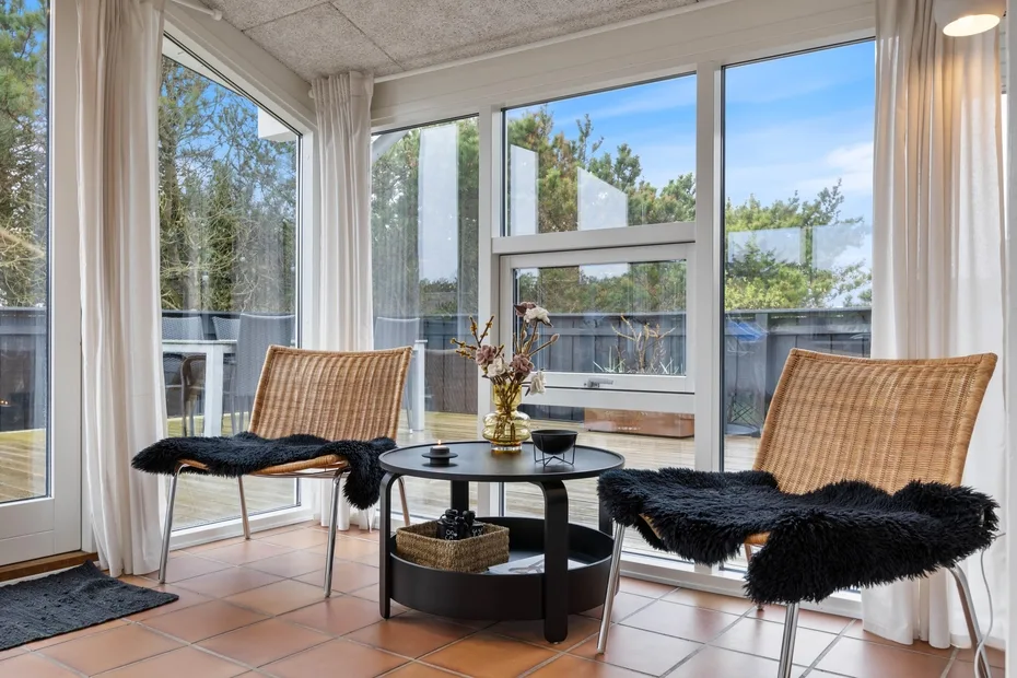 A sunlit enclosed sitting area with large windows and two wicker seats.
