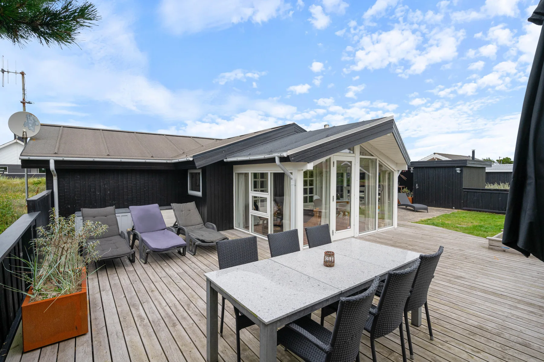 A wooden deck with outdoor seating and a dining table beside a modern house.
