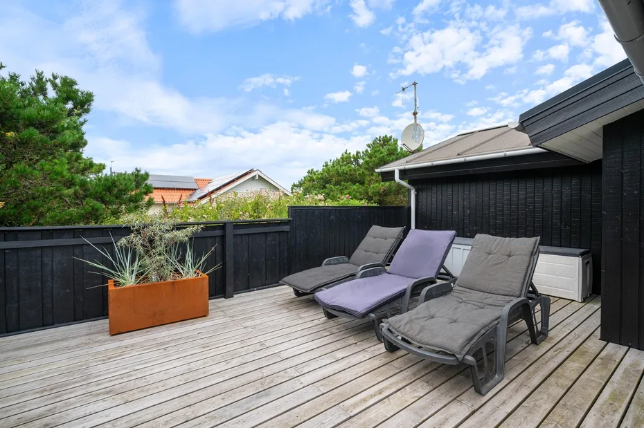 An outdoor deck with reclining lounge chairs and planters beside a black exterior wall.