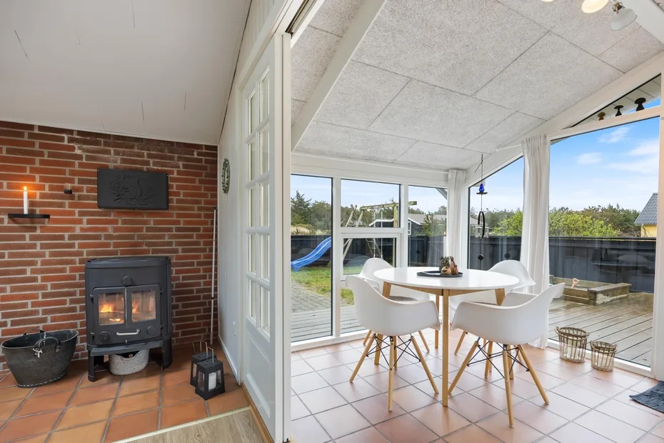 A sunlit dining area with a round table and large windows overlooking a deck.