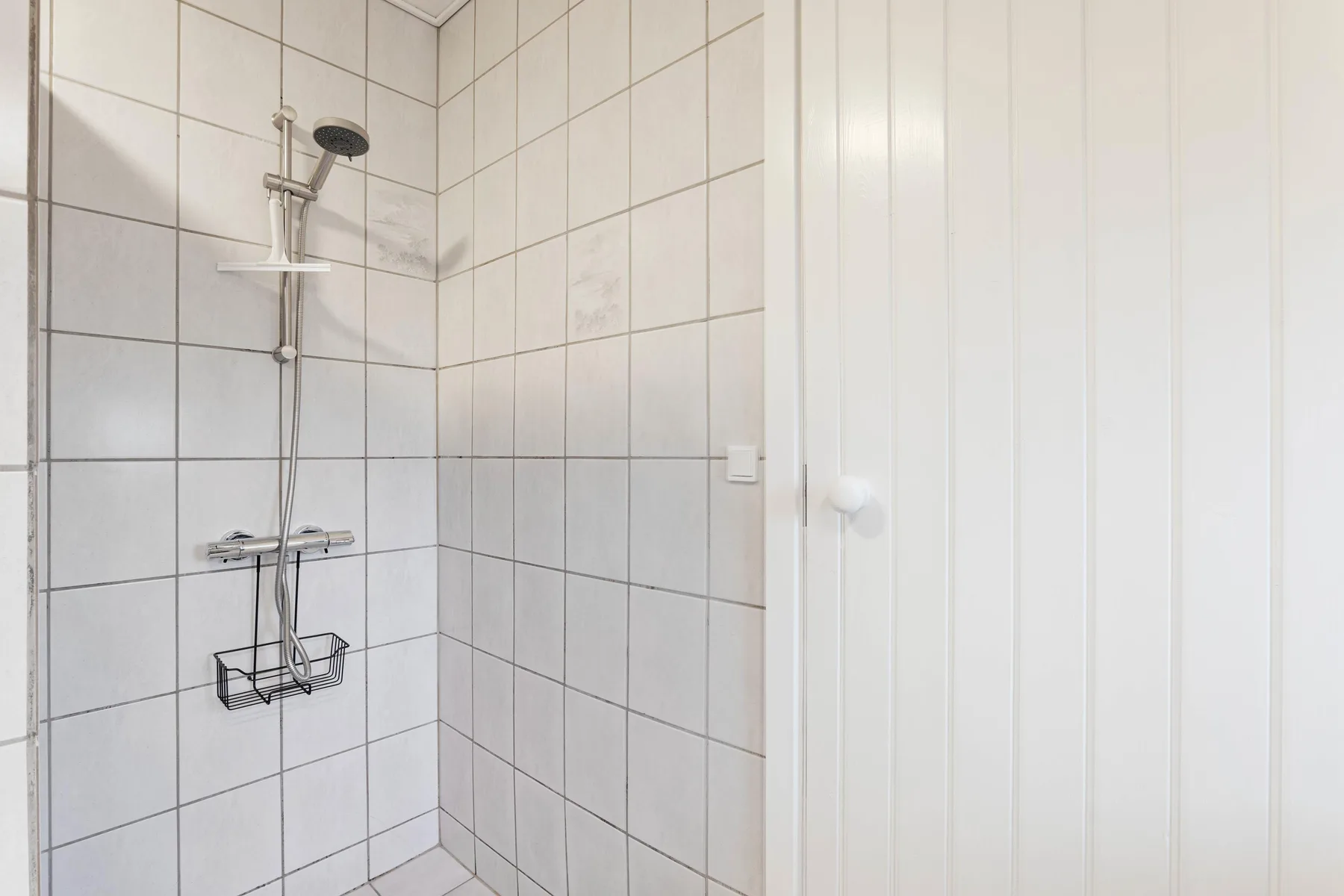 A tiled shower area with a wall-mounted showerhead and controls.