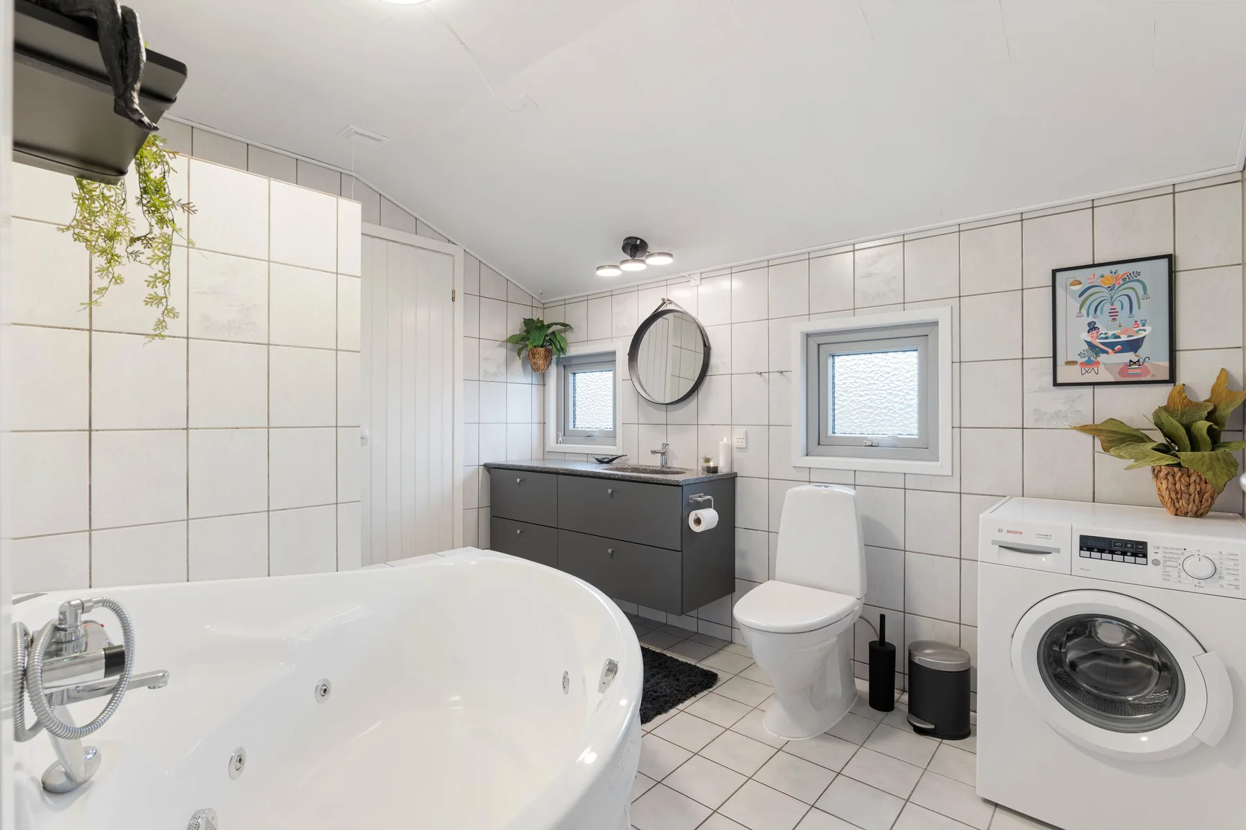 A tiled bathroom with a bathtub, vanity, toilet, and washing machine.
