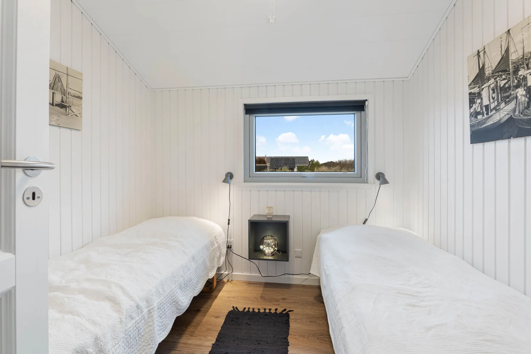 A bright bedroom with two single beds and a window overlooking rooftops.