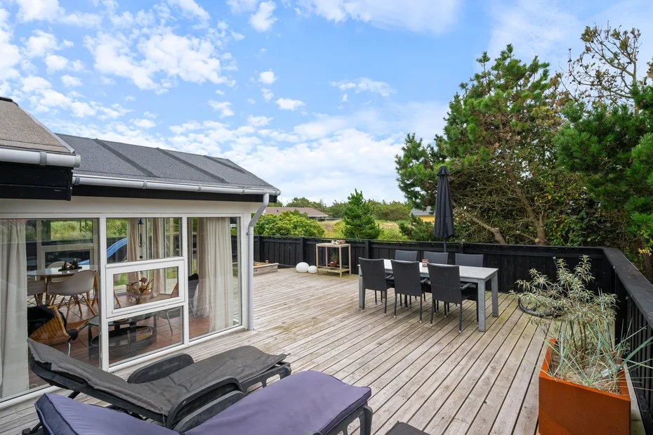 A wooden deck beside a glass-walled living area, with outdoor seating and lounge chairs.