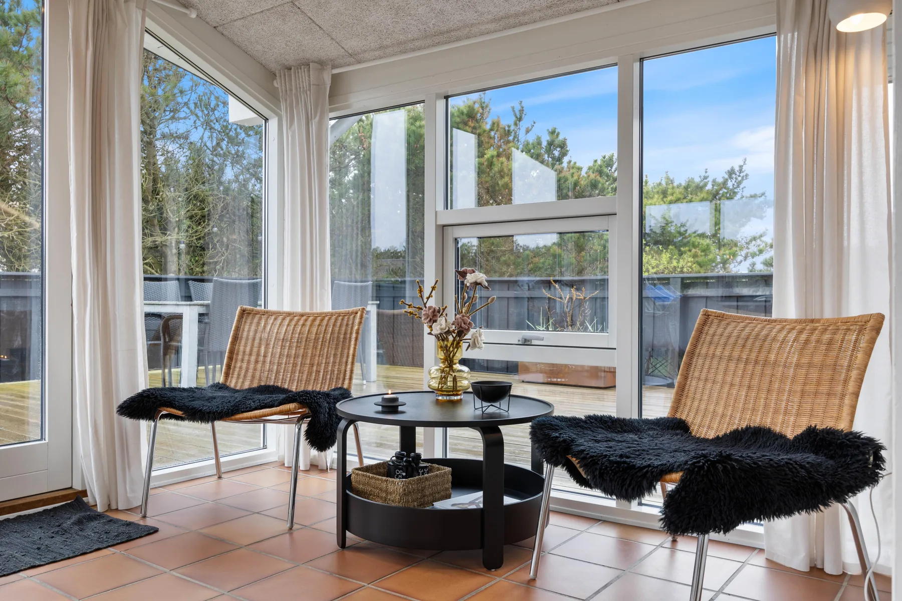 A bright sunroom with wicker seating and a round coffee table beside large windows.