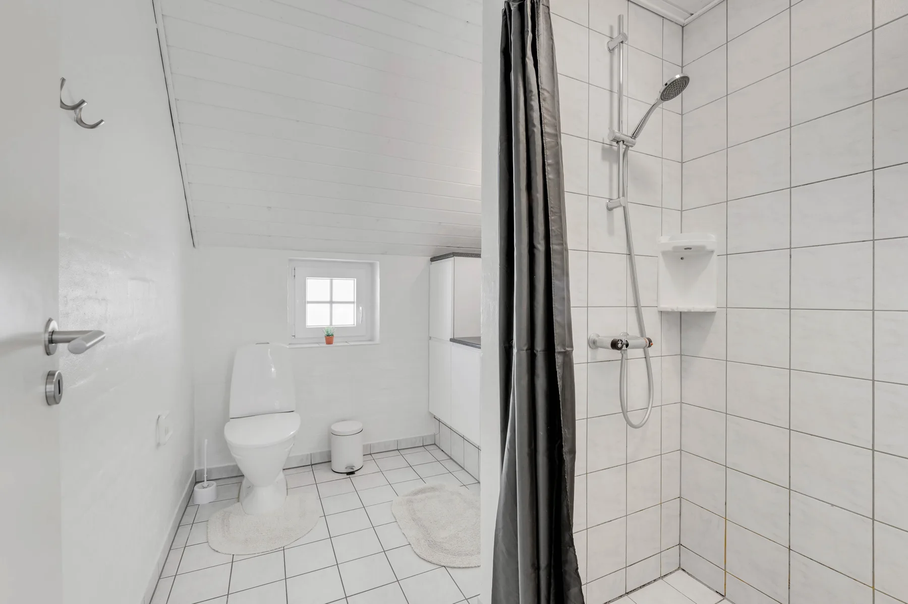 Baño con azulejos, inodoro, lavabo y ducha con cortina.