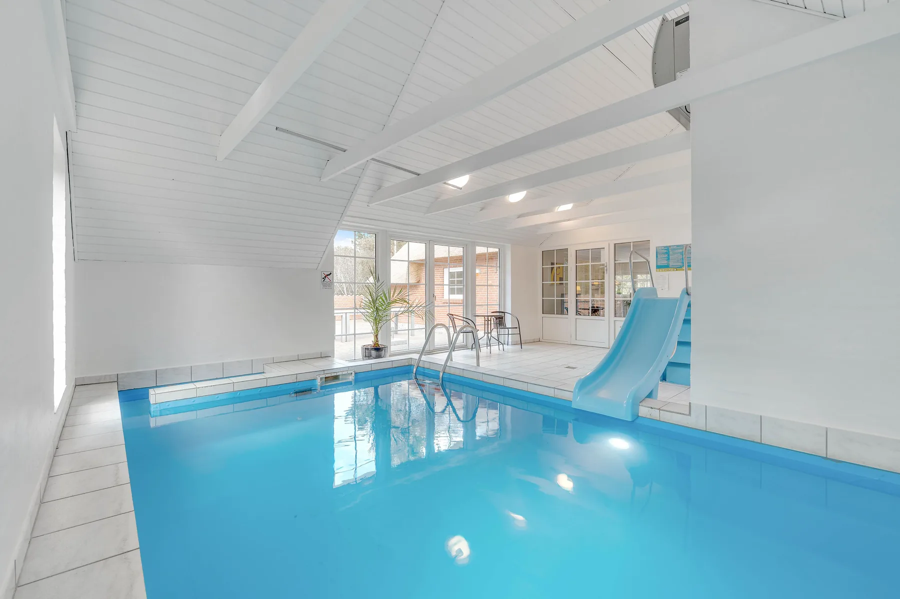 Una piscina cubierta con un tobogán azul bajo un techo blanco inclinado.