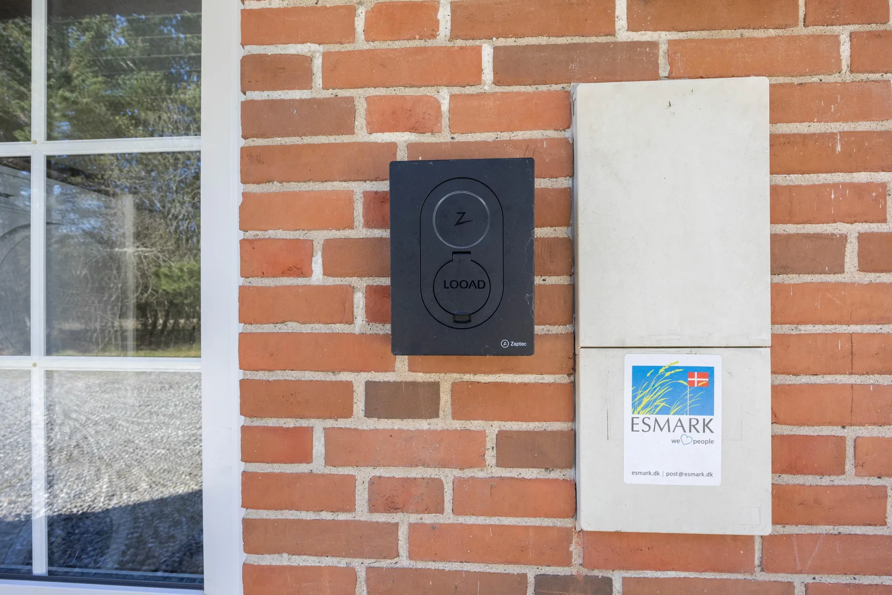 Una pared exterior de ladrillo junto a una ventana tiene un panel de control y un letrero.