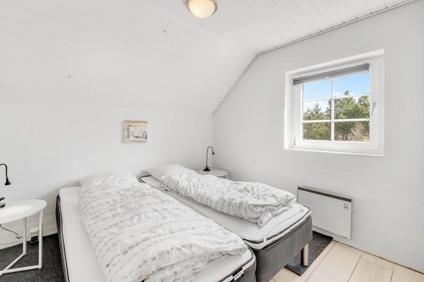 Un dormitorio luminoso con dos camas bajo un techo inclinado y una ventana.