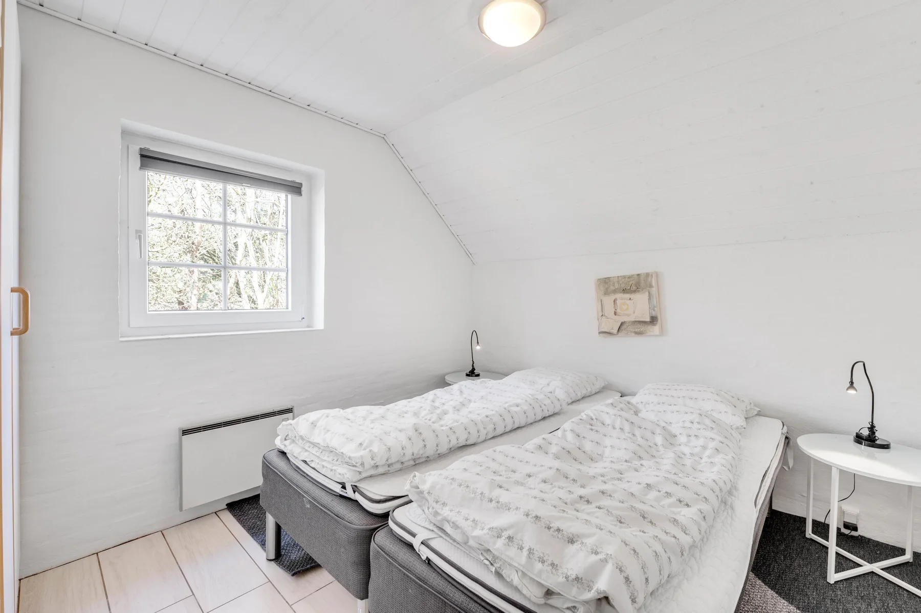 Dormitorio con dos camas, una ventana y una mesita de noche.