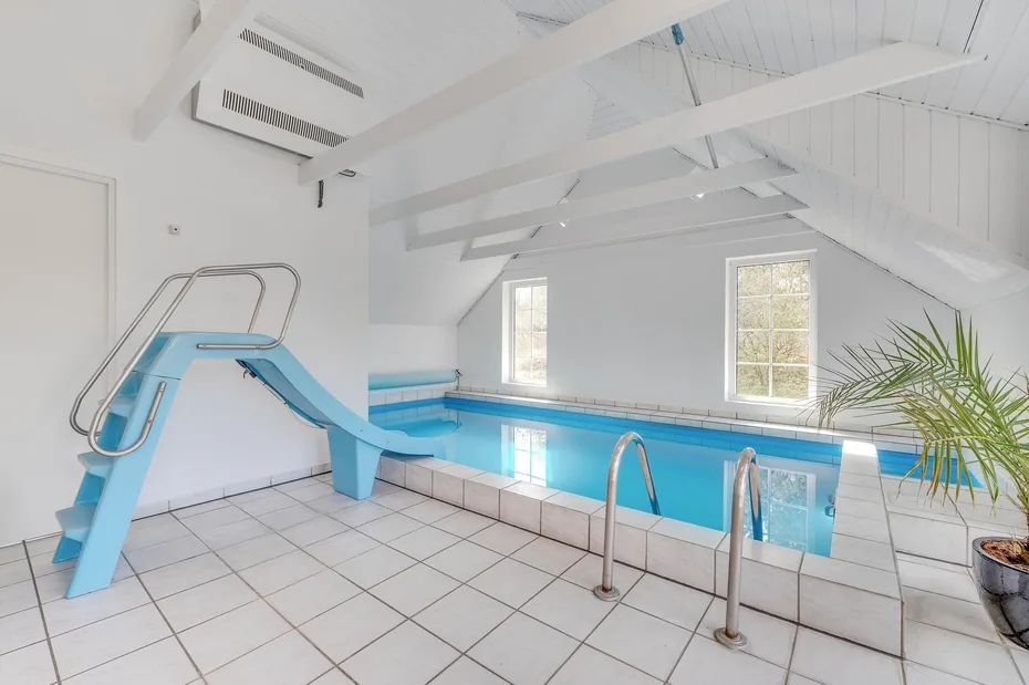 Una piscina cubierta tiene un tobogán azul y suelo de baldosas blancas.