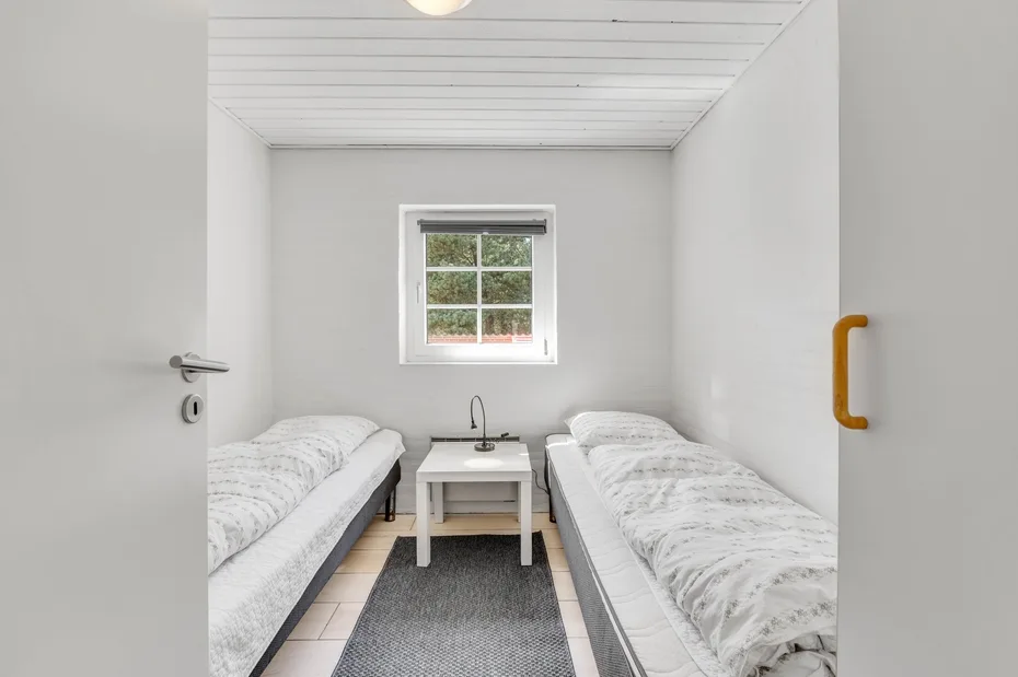 Un dormitorio luminoso con dos camas y una mesita bajo la ventana.