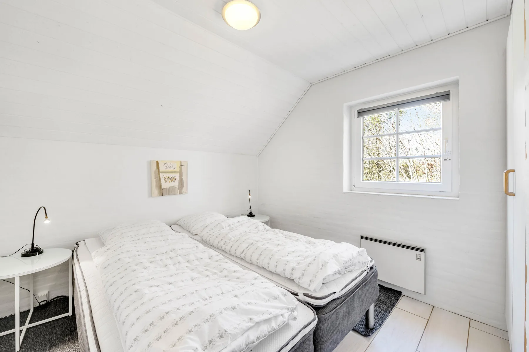 Dormitorio luminoso con dos camas y una ventana con vistas a los árboles.