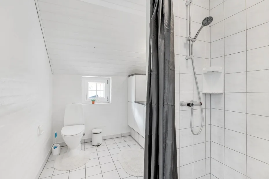 Un baño luminoso con inodoro, zona de lavabo y ducha con azulejos.