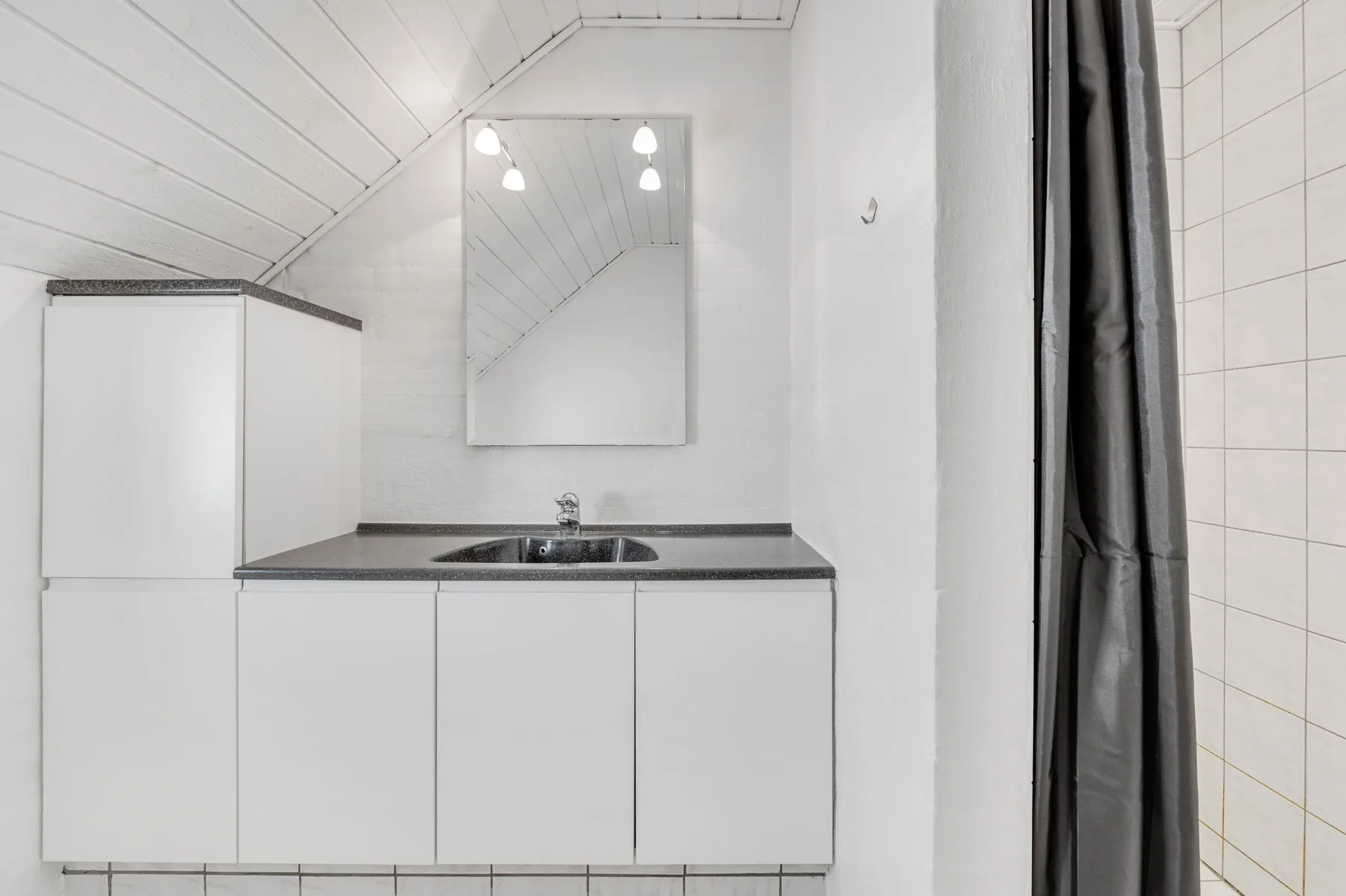 Un lavabo de baño con espejo bajo un techo inclinado.