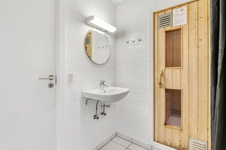 Un baño luminoso con lavabo de pared, espejo redondo y puerta de madera.